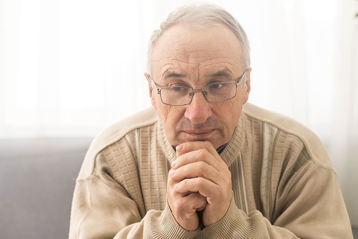 Thoughtful elderly man wearing glasses and beige sweater reflecting on surprising body quirks and unique personal traits.
