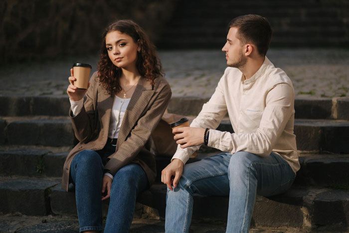 Young woman holding coffee, sitting with man on steps, illustrating lady framing SIL and turning brother against wife.