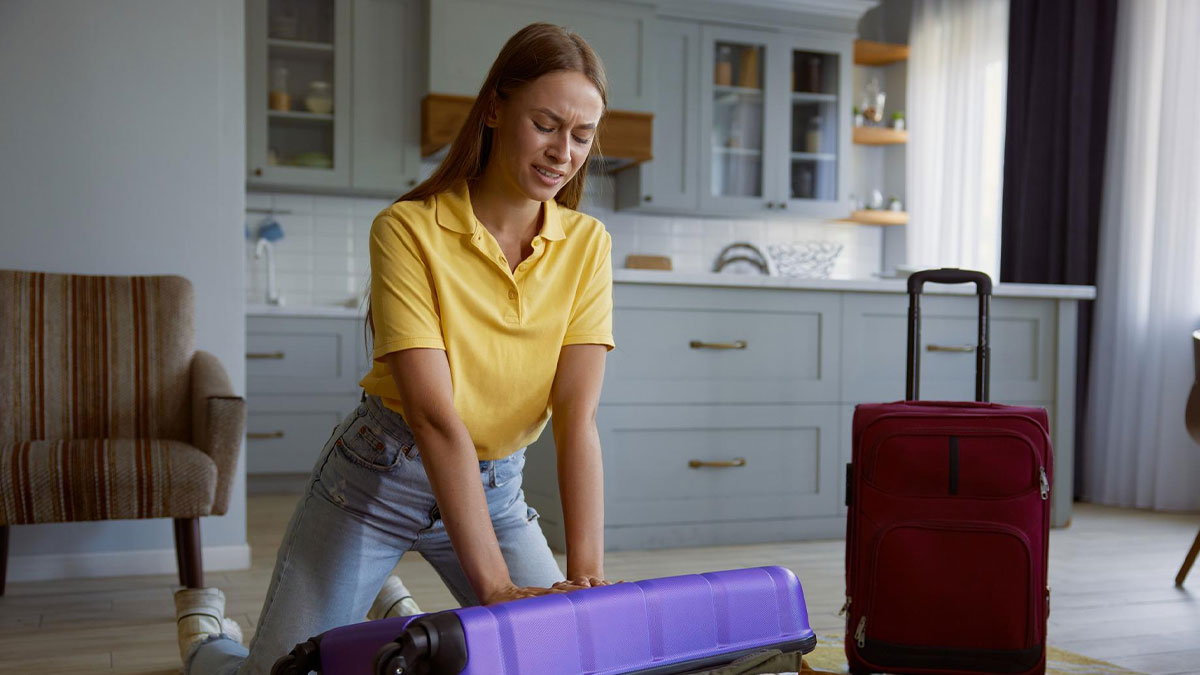 Woman in yellow shirt kneeling by suitcase, upset and stressed, illustrating lady framing SIL and turning bro against wife.