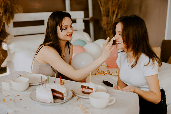Two women celebrating a birthday with cake and balloons, highlighting a husband’s birthday surprise leading to therapy. Two women celebrating a birthday with cake and balloons, highlighting a husband’s birthday surprise leading to therapy.