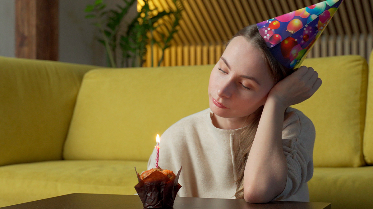 Woman in a birthday hat looking disappointed at a cupcake with candle, reflecting on husbandu2019s birthday surprise and marriage issues.