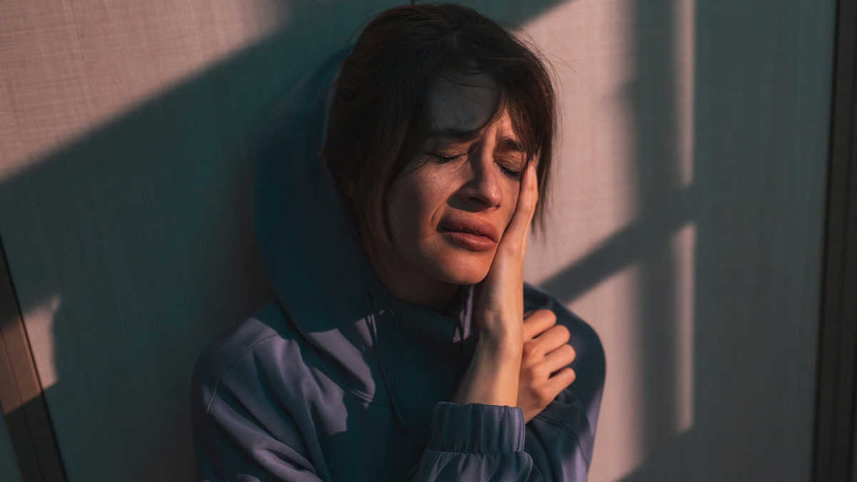 Claustrophobic woman in tears, distressed and upset, sitting alone in dim light after a prank causing emotional pain.