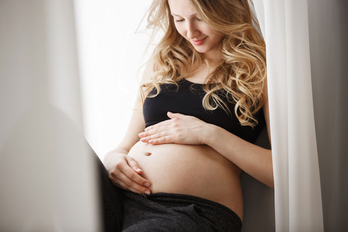 Pregnant woman smiling gently while sitting by the window, holding her belly and embracing her pregnancy moment. Pregnant woman smiling gently while sitting by the window, holding her belly and embracing her pregnancy moment.