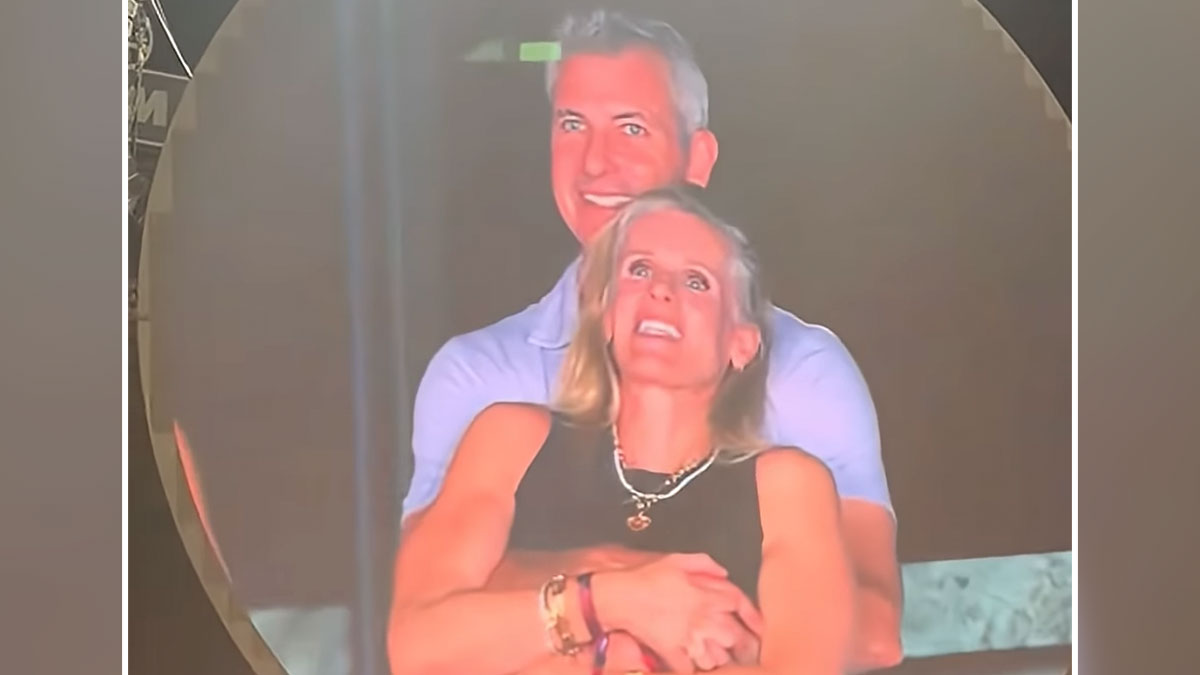Couple embracing warmly on a large screen at a Coldplay concert with husband sympathizing cheaters vibe.