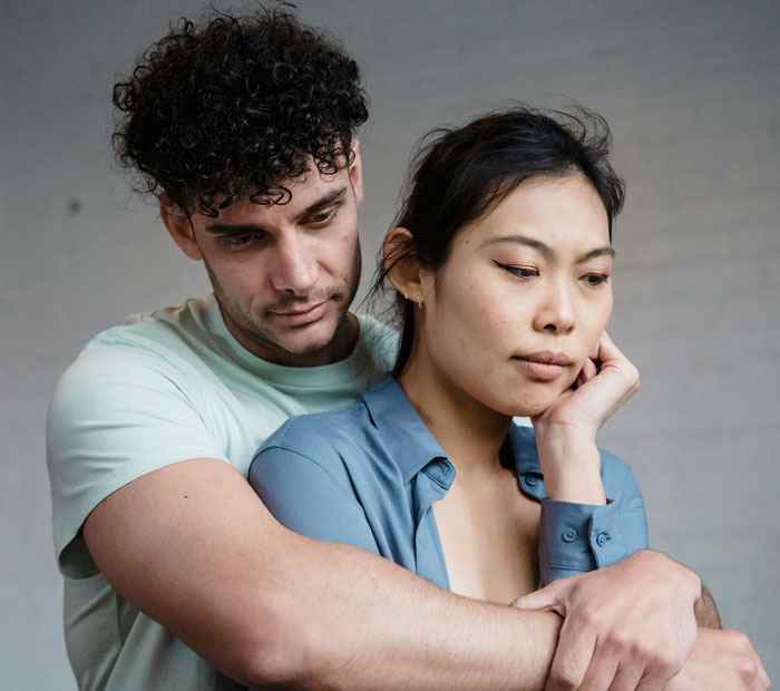 Husband and wife in a tense embrace, wife looking concerned while husband tries to comfort her in a casual setting. Husband and wife in a tense embrace, wife looking concerned while husband tries to comfort her in a casual setting.