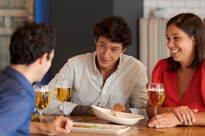 Three people sharing drinks and food at a table, highlighting a friend’s compliment turning uncomfortable moment. Three people sharing drinks and food at a table, highlighting a friend’s compliment turning uncomfortable moment.