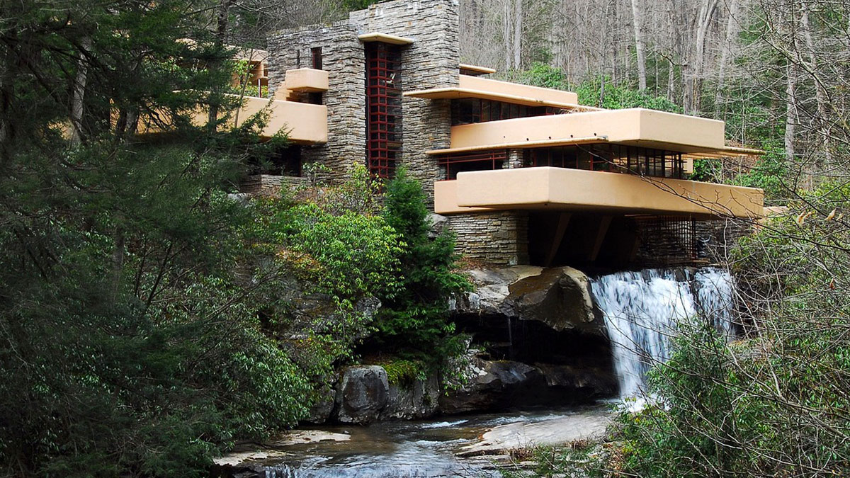 Iconic architectural home built over a waterfall, surrounded by lush forest and rocky landscape.