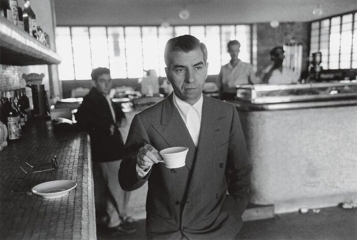 Black and white photo of a mob boss in a suit holding a cup in a vintage bar, symbolizing notorious mob bosses.