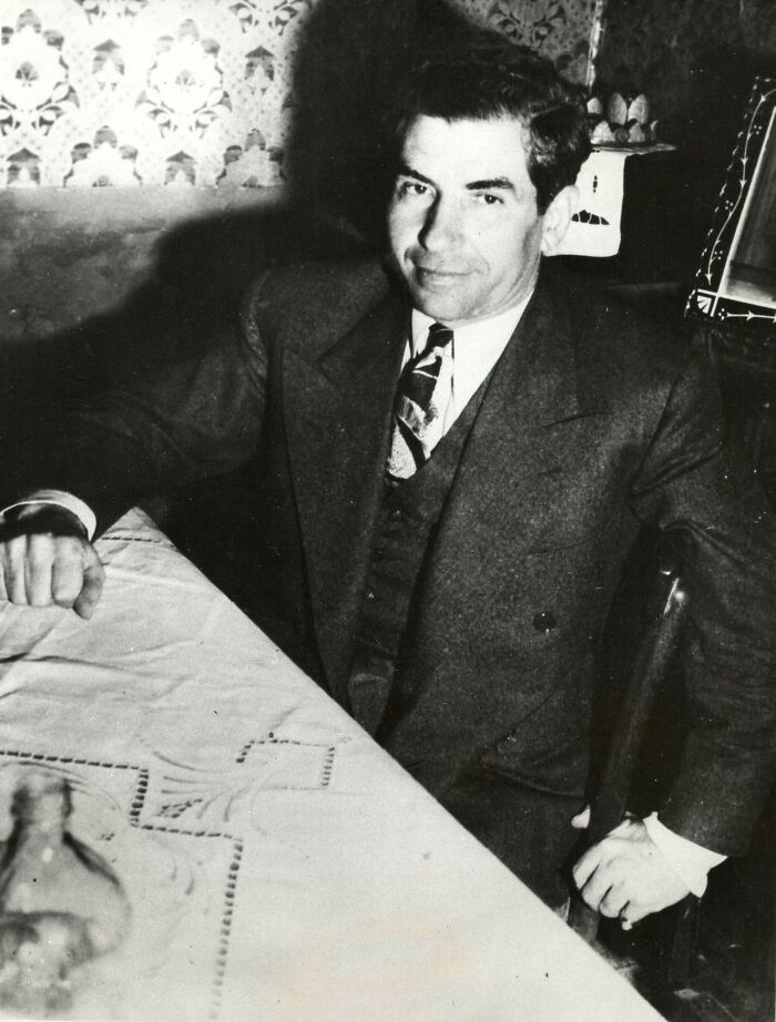 Black and white photo of a mob boss from the mid-20th century sitting at a table, representing notorious mob bosses.