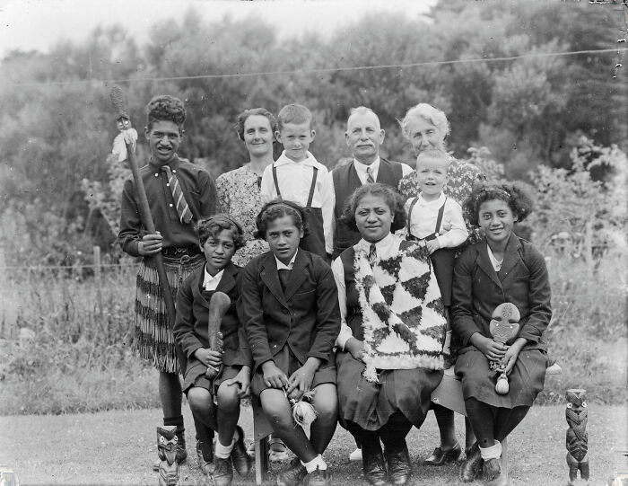 Group portrait of Māori life from a century ago showing children and adults in traditional and formal attire outdoors.