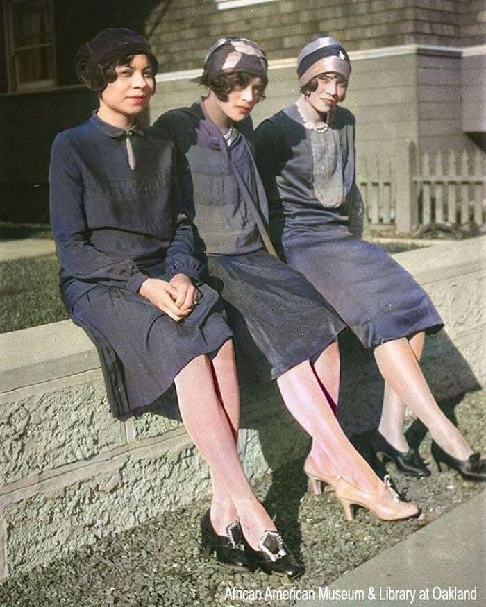 Three African American women in 1920s dresses and hats sitting outdoors, showcasing the African American reality of the era.