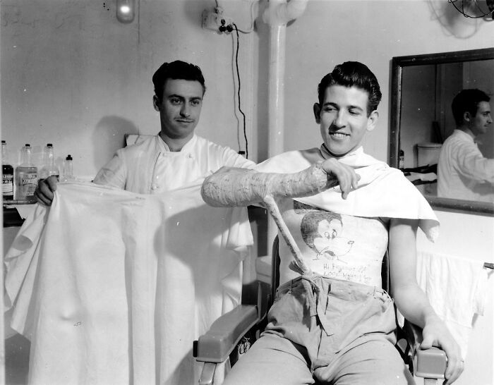 Young WWII soldier with a large arm cast smiling at a barber in a vintage black and white photo rare WWII photos