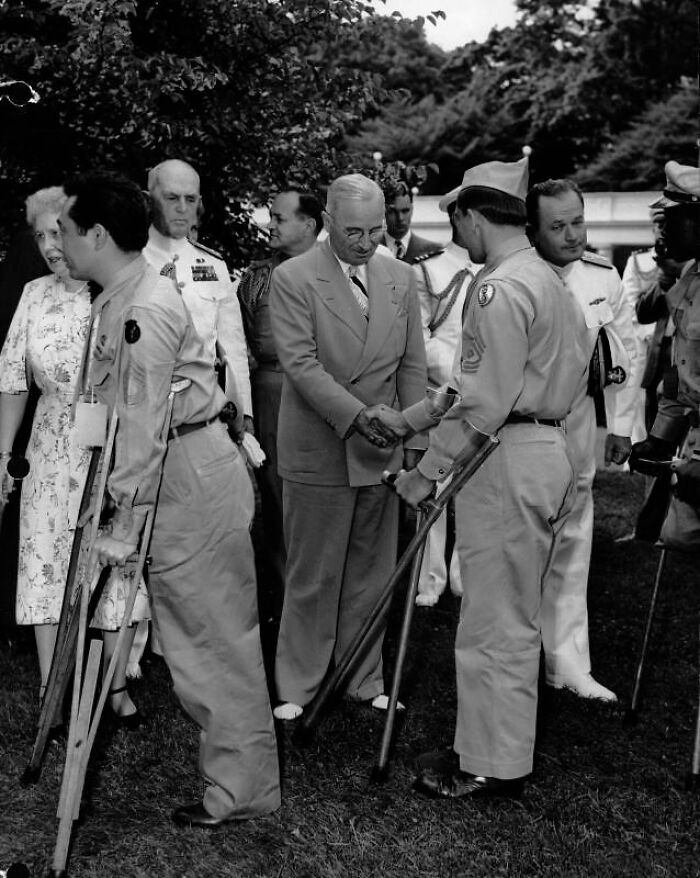 President Harry Truman shaking hands with wounded WWII soldiers on crutches during a rare WWII photo opportunity outdoors.