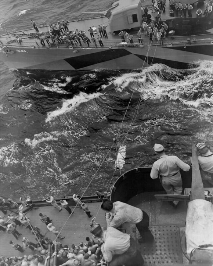 Rare WWII photo showing sailors on two naval ships transferring supplies over choppy ocean waters during wartime operations.