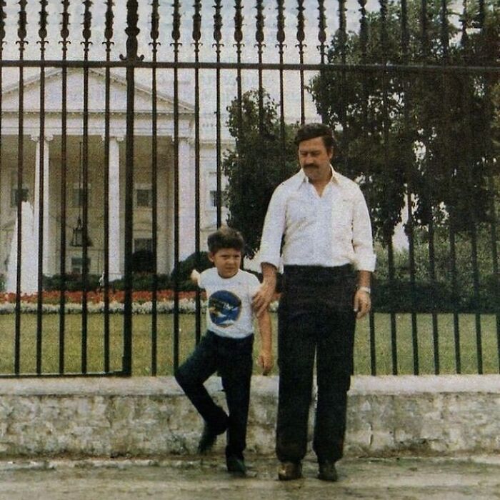 Mob boss with young boy standing outside iron gate near famous government building, representing notorious mob bosses.