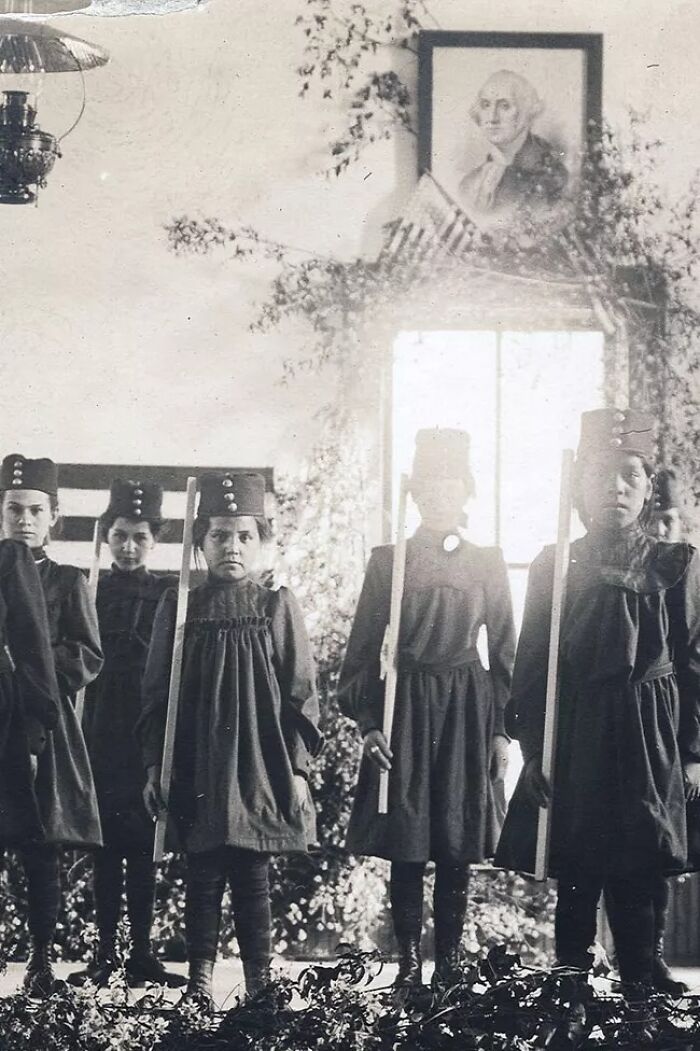 Group of Native American girls in uniform holding wooden rifles at a boarding school in the 1910s.