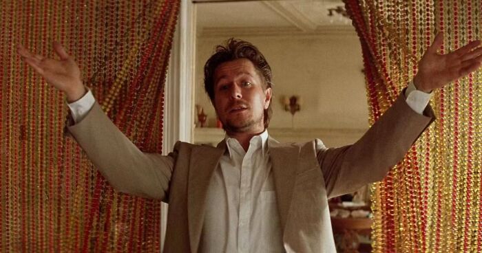 Actor in beige suit with open arms standing between beaded curtains in iconic heartthrob photo from classic film scene.