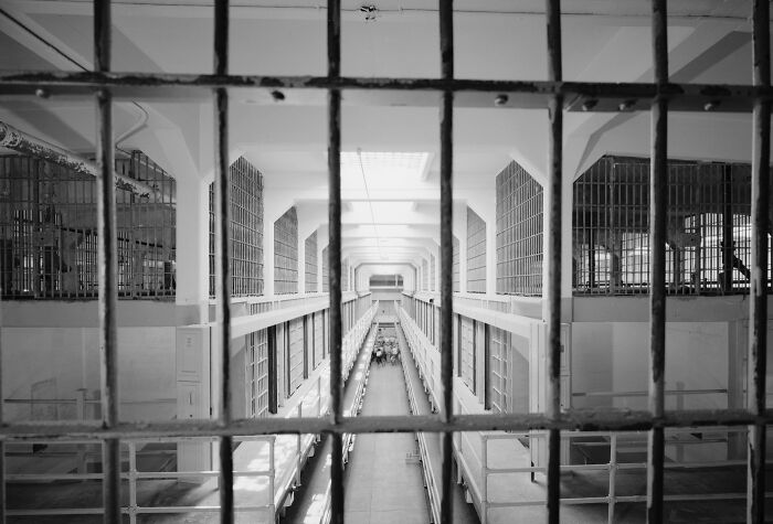 View through bars into a long, empty Alcatraz prison cell block, showing the harsh reality of life on Alcatraz.