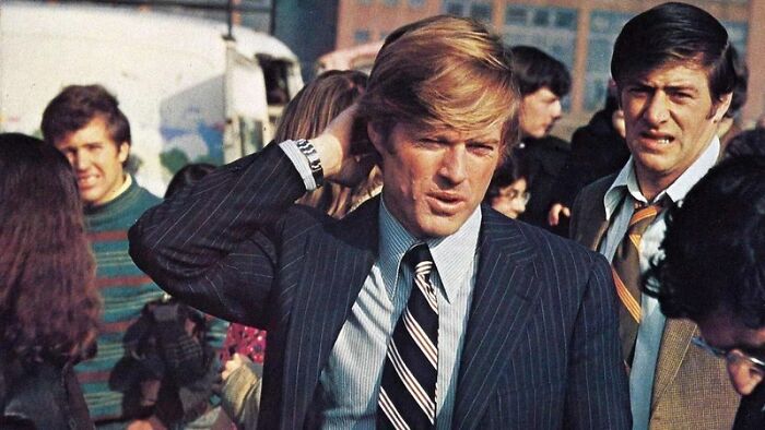 Actor in a pinstripe suit and striped tie among a crowd, captured as an iconic heartthrob of his time.