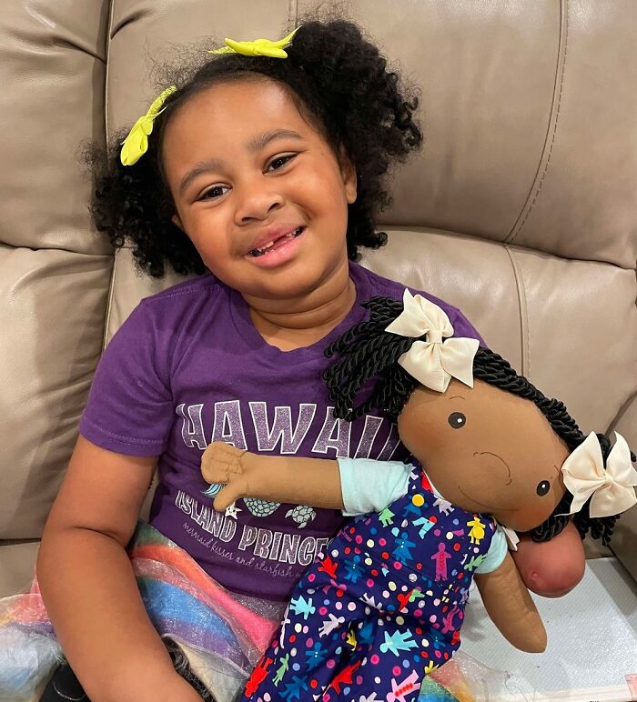 Young girl smiling on couch holding a custom doll designed to represent rare health conditions in children.