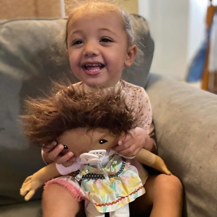 Young girl smiling while holding a custom doll designed to represent rare health conditions and individual needs.