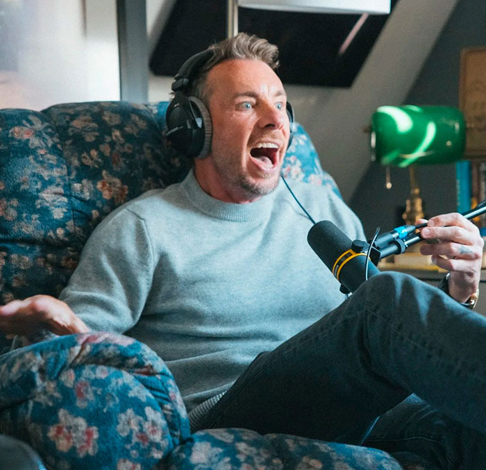 Dax Shepard wearing headphones, speaking into a microphone, reacting excitedly during a podcast recording session. Dax Shepard wearing headphones, speaking into a microphone, reacting excitedly during a podcast recording session.