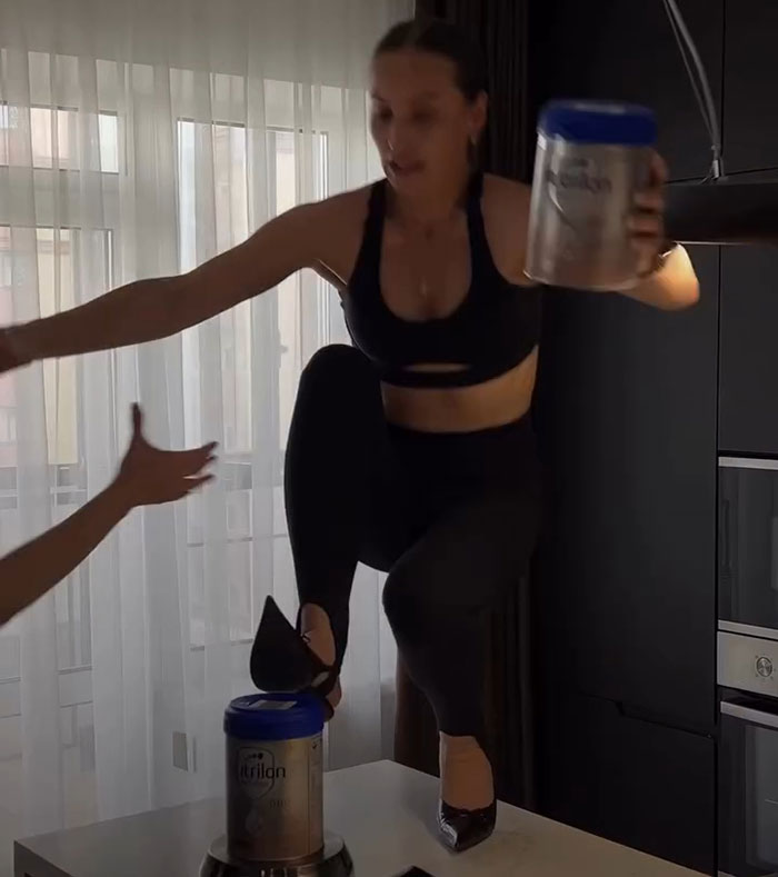 Influencer attempting Nicki Minaj stiletto challenge wearing heels and black workout outfit inside a modern kitchen. Influencer attempting Nicki Minaj stiletto challenge wearing heels and black workout outfit inside a modern kitchen.