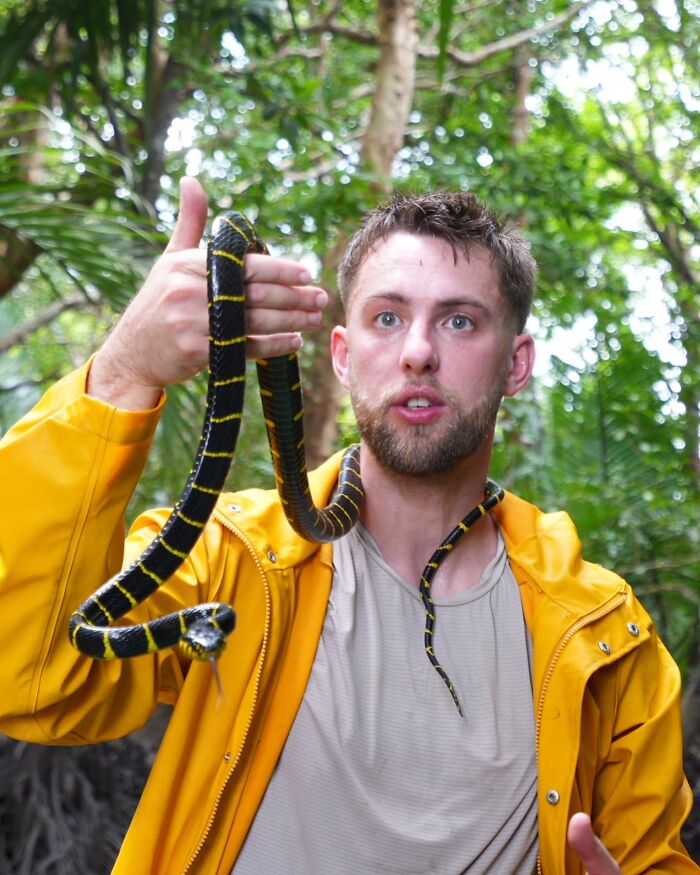 Man in a yellow jacket holding a black and yellow snake, highlighting influencer sparks outrage filming indigenous tribe controversy. Man in a yellow jacket holding a black and yellow snake, highlighting influencer sparks outrage filming indigenous tribe controversy.