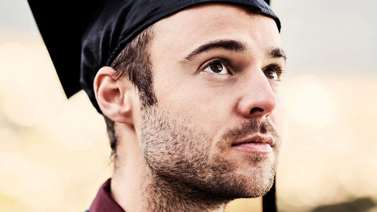 Young man in graduation cap looking up thoughtfully, symbolizing curiosity and delight in new facts discovery.