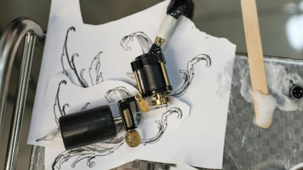Close-up of a tattoo machine resting on paper with ink sketches, showcasing ingenious inventions repurposed creatively.