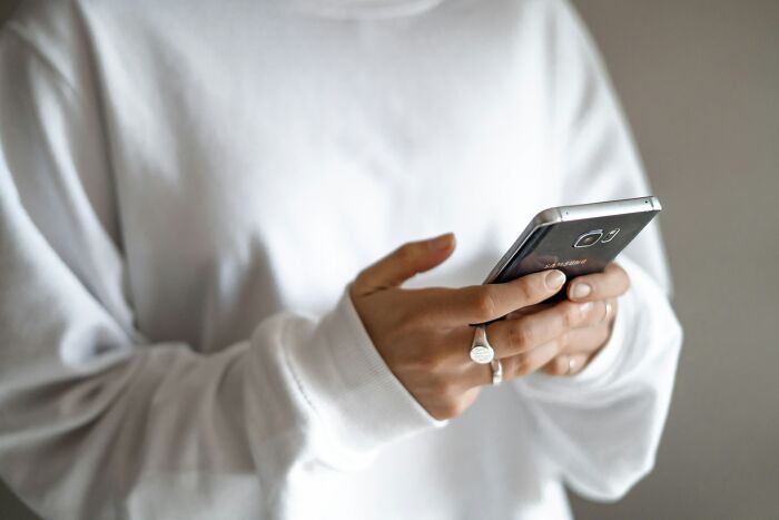 Person wearing white sweater holding a smartphone, representing performative behaviors people expose in society today.
