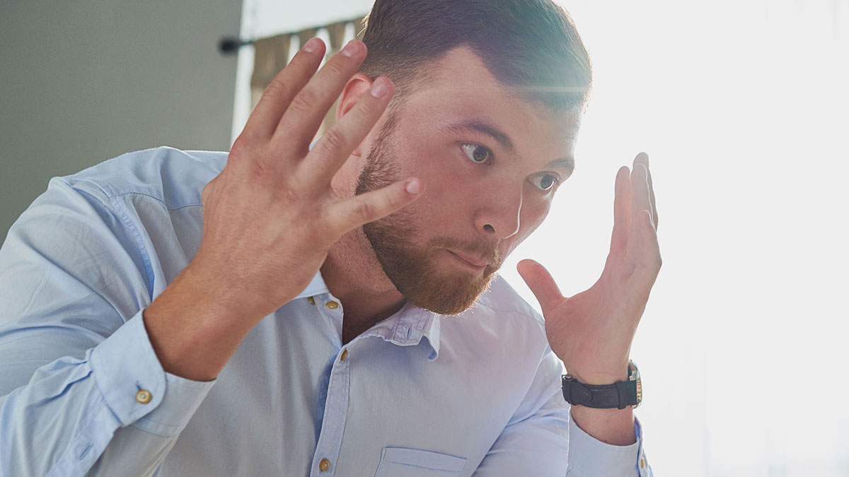 Man in light blue shirt raising hands, showing frustration related to host kicking out neurodivergent buddy after hearing aids incident