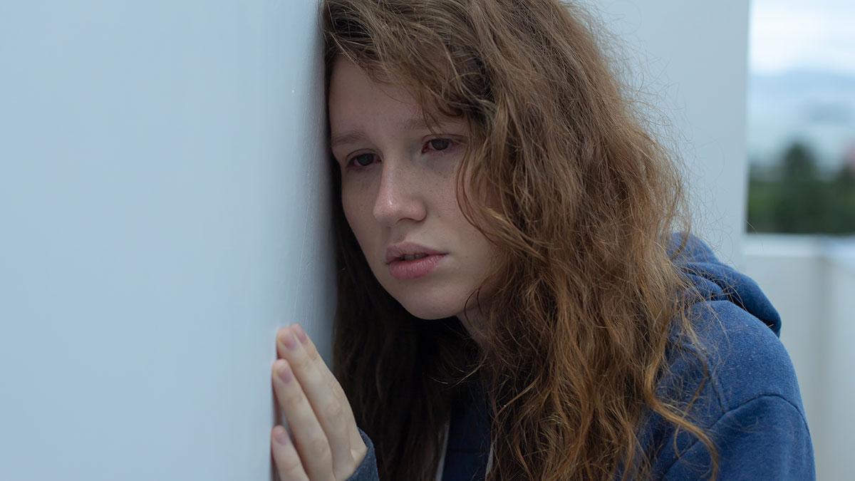 Young woman with long hair leaning against a wall, appearing distressed and reflecting on kidnapping survival experiences.