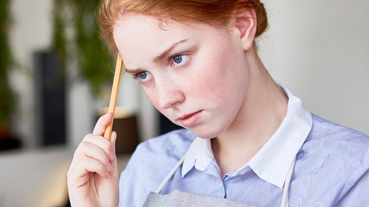 Thoughtful young woman holding a pencil to her head, reflecting on parents leaving kid unattended in pet store damages.