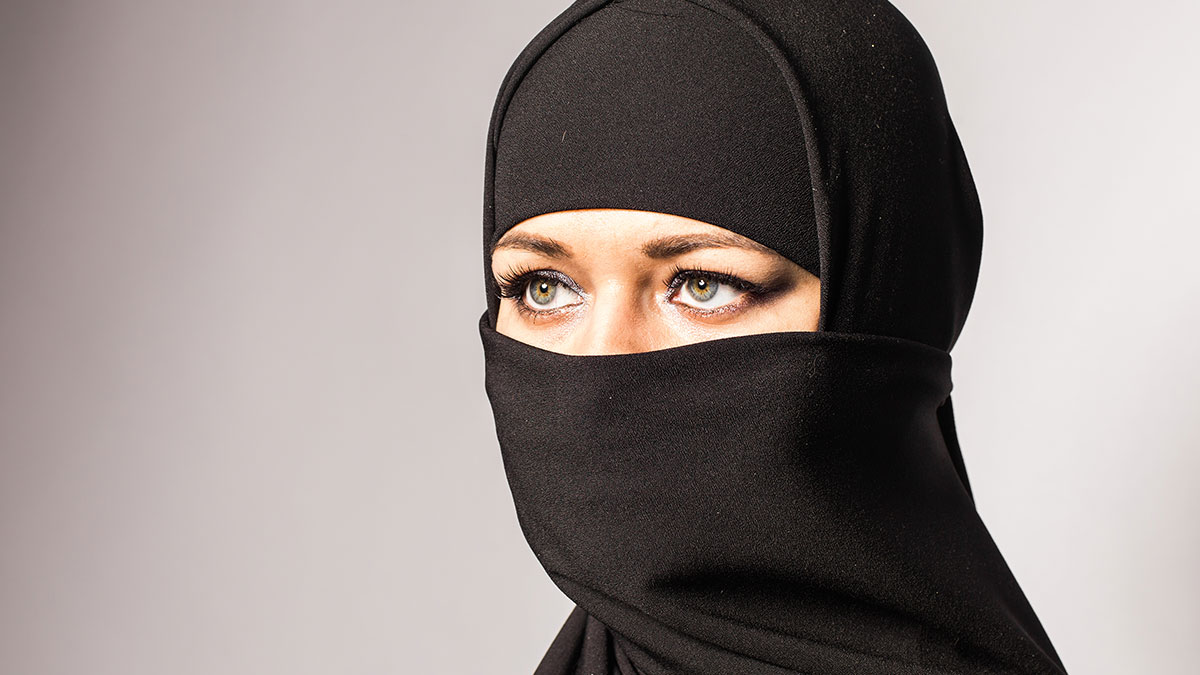 Woman wearing black niqab covering her face, highlighting eyes and expression on a neutral background.