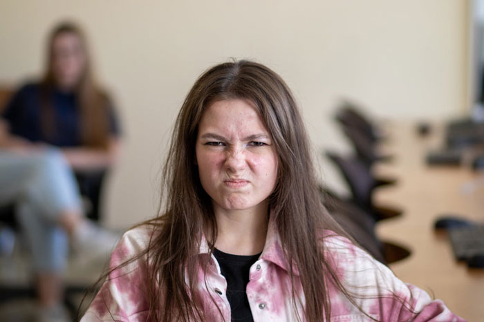 Teen girl making a frustrated face while sitting in a classroom, symbolizing tension with fiancee’s kids. Teen girl making a frustrated face while sitting in a classroom, symbolizing tension with fiancee’s kids.