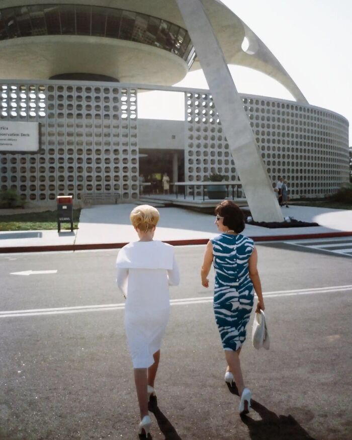 Two LA women walking near a modernist building, dressed stylishly, capturing vintage 1960s lifestyle in 1962.
