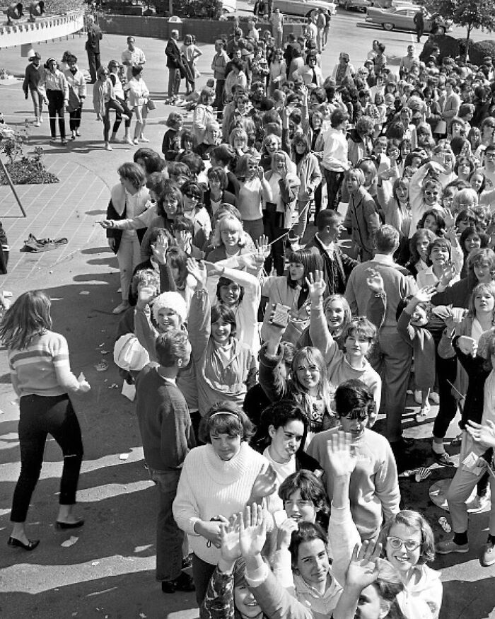 Large crowd of LA women in 1960s fashion, happily waving and socializing outdoors, capturing vibrant women living their best lives.