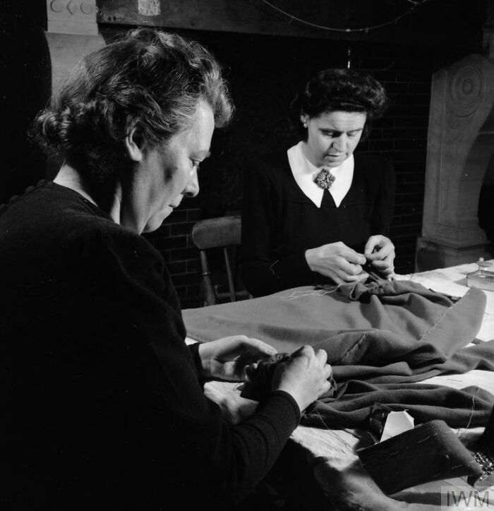 Two British women sewing and mending clothes during WWII, showcasing how British women kept their style despite restrictions.