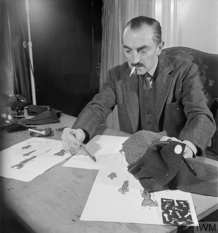 Man sketching fashion designs at a table, surrounded by fabric samples showing how British women kept style during WWII restrictions.
