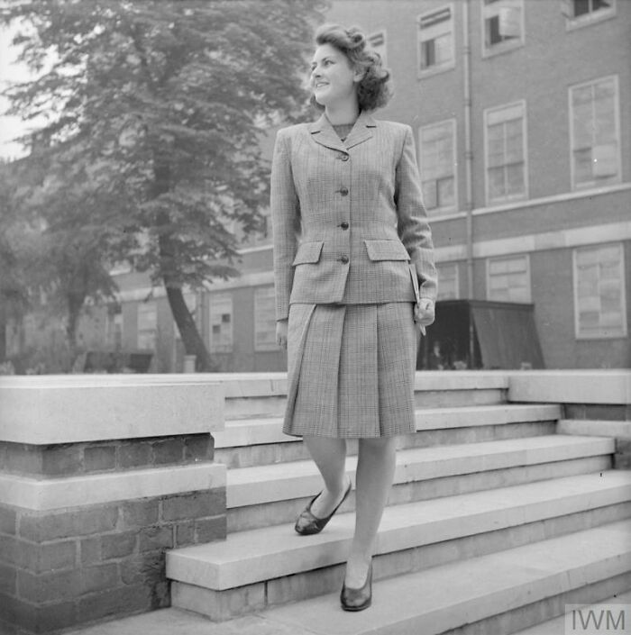British woman in a tailored suit walking down steps, showcasing WWII style and fashion during wartime restrictions.