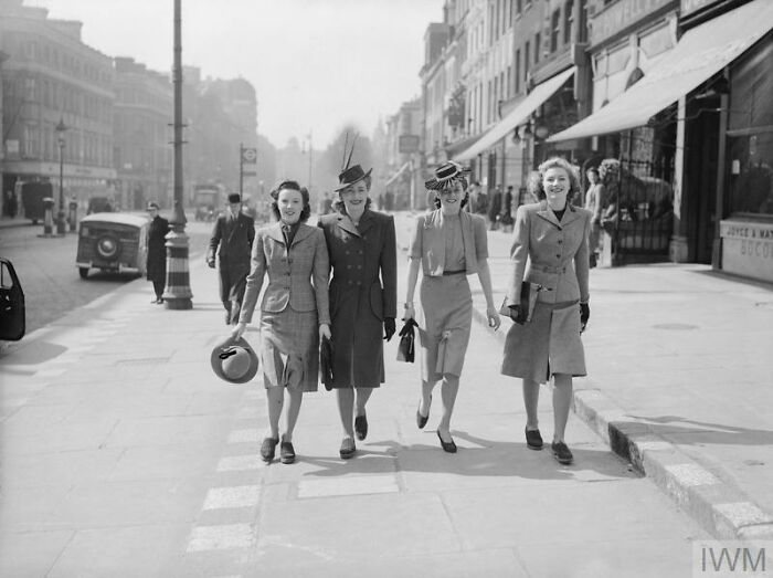Four British women dressed in stylish wartime fashion walking confidently on a city street during WWII restrictions.