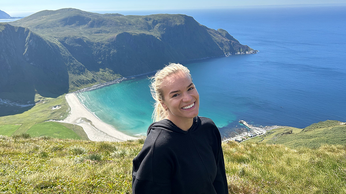 Young woman smiling in front of scenic coastal cliffs and ocean, symbolizing a one-way flight to Australia journey.