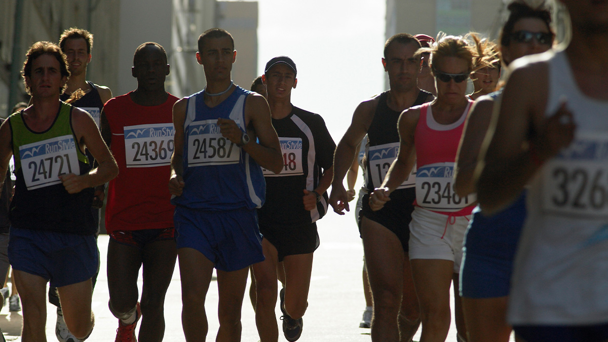 Runners with numbered bibs competing in the Boston Marathon on a bright day, focused on their race pace.