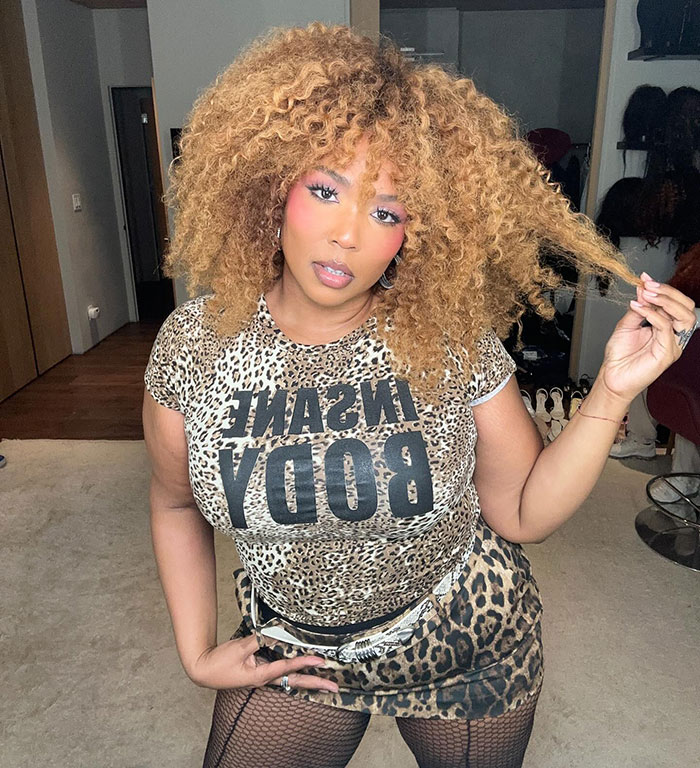 Lizzo in leopard print outfit, posing indoors with voluminous curly hair, referencing Sydney Sweeney ad controversy parody. Lizzo in leopard print outfit, posing indoors with voluminous curly hair, referencing Sydney Sweeney ad controversy parody.