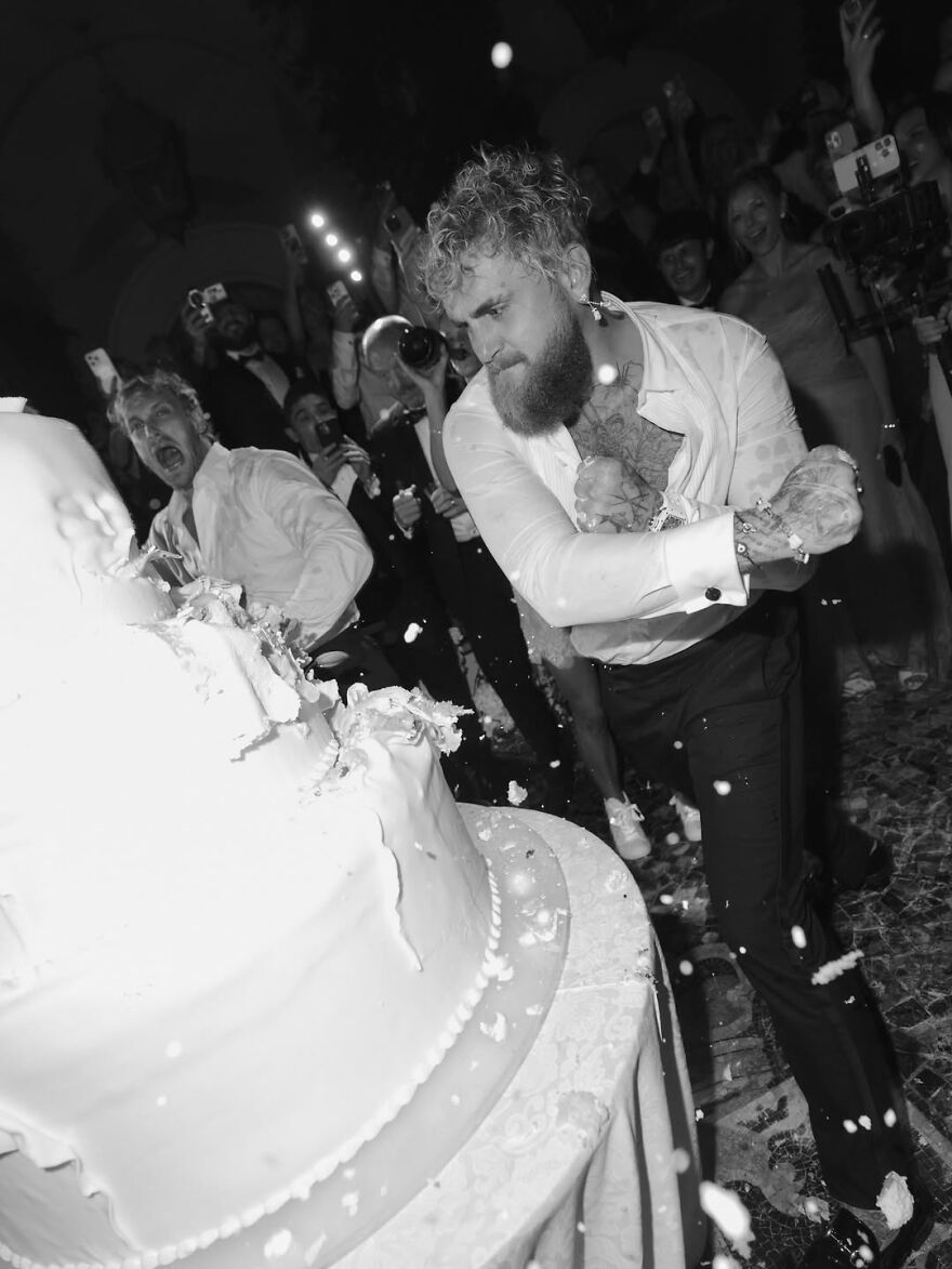 Jake Paul smashing wedding cake at event with crowd reacting and capturing the bizarre viral moment in black and white. Jake Paul smashing wedding cake at event with crowd reacting and capturing the bizarre viral moment in black and white.