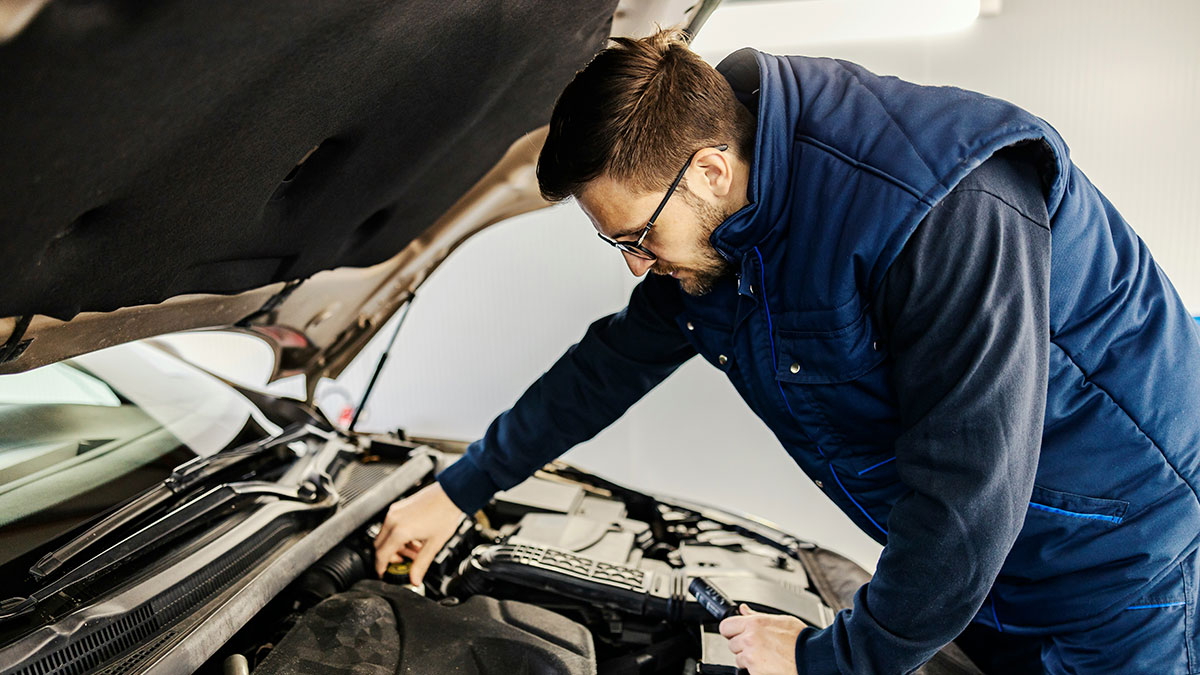 Man wearing glasses and a blue vest inspecting car engine, demonstrating people accidentally discovered loopholes use.