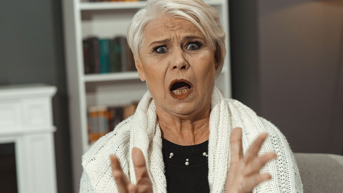 Older woman expressing shock and frustration indoors, illustrating conflict over widow moving back to home country with kids.