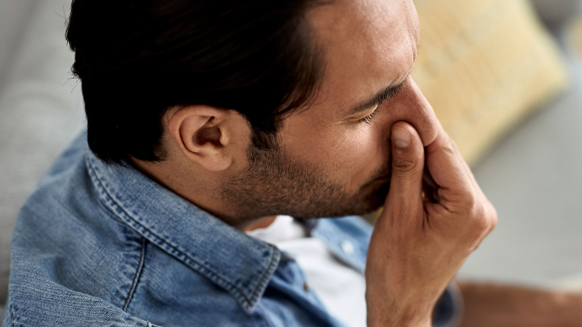 Man in denim shirt pinching nose, reacting to nasty scents while family hosts divorcing friend at home.