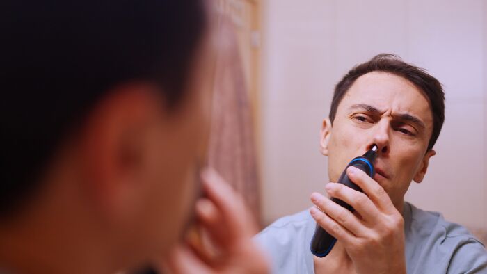 Man using an electric nose hair trimmer in a bathroom, highlighting unexpected items on wedding registries.